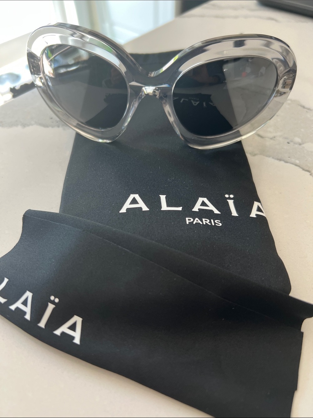 Alaïa Paris Clear Oval Sunglasses with Dark Lenses